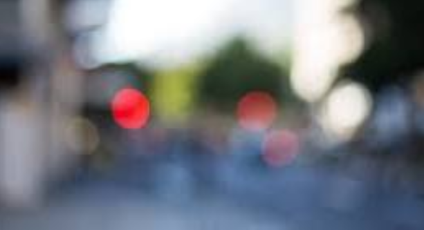 Blurry street scene featuring a prominent red traffic light against an indistinct background.