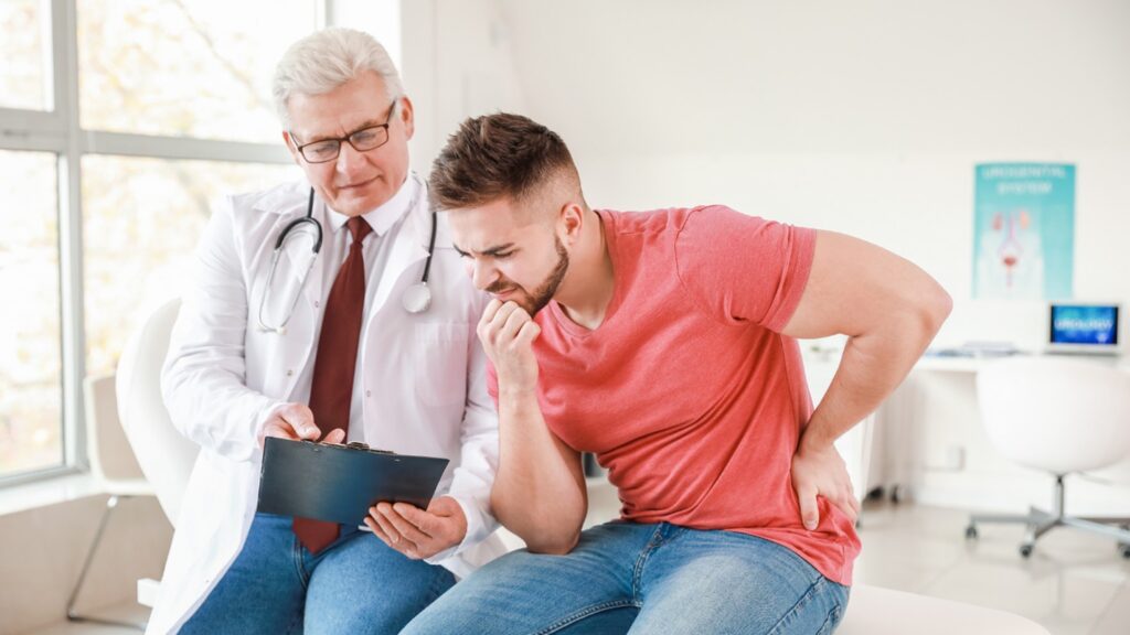 A Mam Holds His Back and Looks at A Doctor's Clipboard