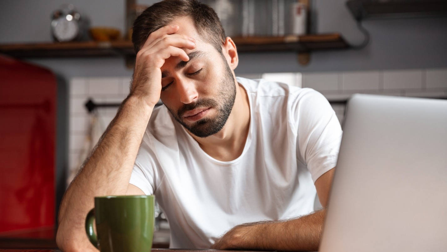 A distressed man sits in front of his laptop.