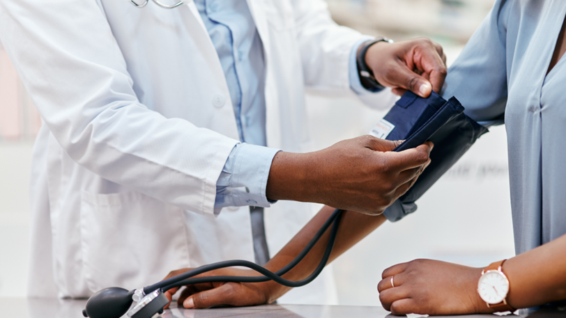 A primary care doctor places a blood pressure cuff on the arm of a patient.