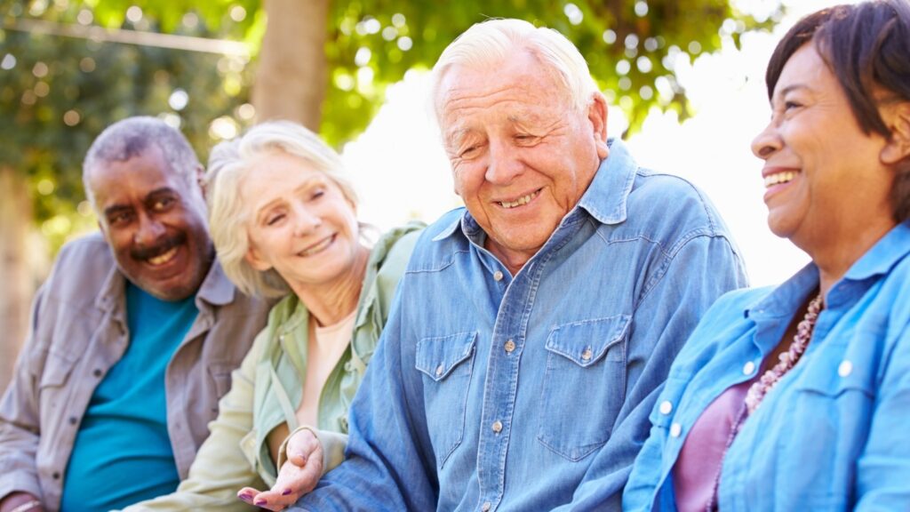 Four senior men and women sit together at a park.