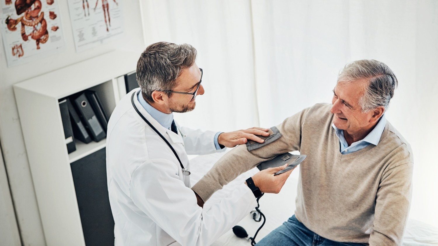 A smiling patient getting a blood pressure check by a primary care doctor.