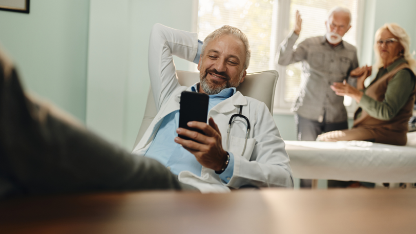 A doctor watches his phone while his patients need help behind him.